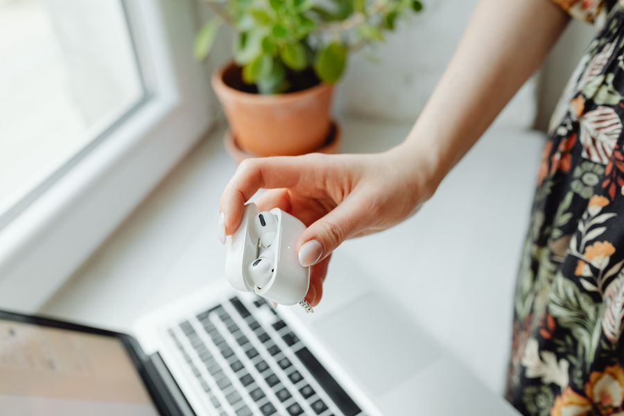 A person holding wireless earbuds over a laptop at a desk